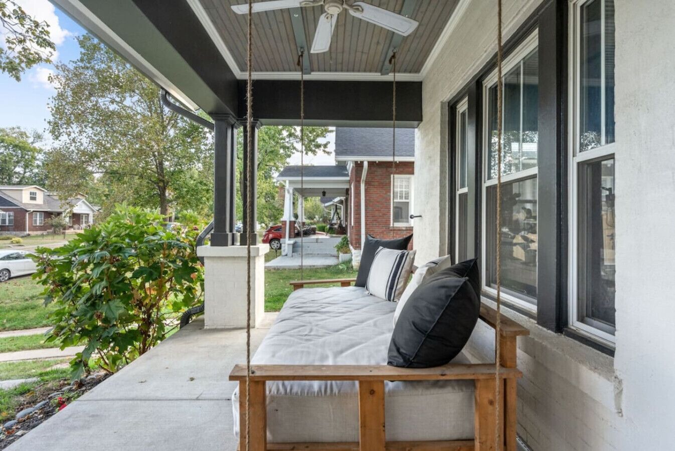 A porch with a wooden bench, a ceiling fan, and a view of a residential street.