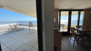 A room with a view of the ocean, a balcony with chairs and a table, and a dining area with chairs and a table. - Gulf Front Condo with Stunning Views! (Pensacola)