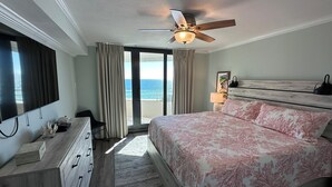 A bedroom with a bed, a ceiling fan, a TV, a dresser, and a view of the ocean. - Gulf Front Condo with Stunning Views! (Pensacola)