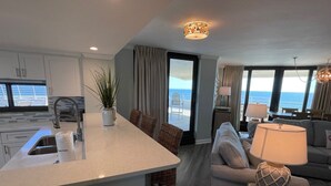 A modern hotel room with a kitchen area, a seating area with a sofa and chairs, and a view of the ocean. - Gulf Front Condo with Stunning Views! (Pensacola)