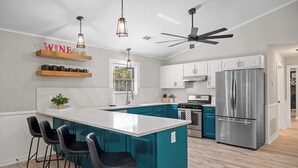 A modern kitchen with teal cabinetry, a large island with bar stools, a stainless steel refrigerator, and pendant lighting. - Fritztown's Finest - Hot Tub, Fire Pit & Sleeps 10 (Fredericksburg)