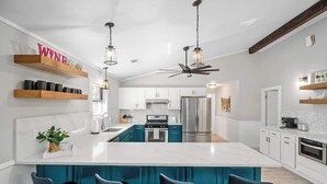 A modern kitchen with a central island, bar stools, and a ceiling fan. - Fritztown's Finest - Hot Tub, Fire Pit & Sleeps 10 (Fredericksburg)