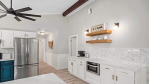 A modern kitchen with white cabinets, a stainless steel refrigerator, a dishwasher, and wooden shelves above the countertop. - Fritztown's Finest - Hot Tub, Fire Pit & Sleeps 10 (Fredericksburg)