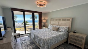 Una camera da letto con un grande letto, una scrivania e una TV. Si apre una vista sull'oceano attraverso ampie finestre.
