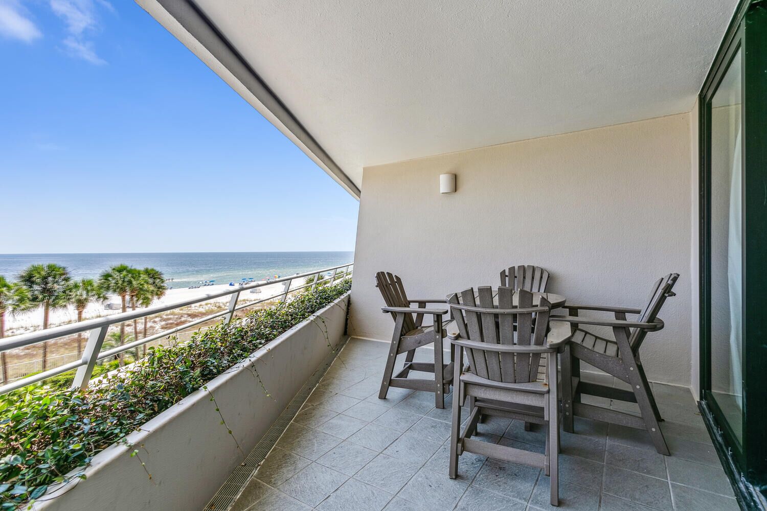 A balcony with a view of the beach, a table with chairs, and a small wall-mounted light.