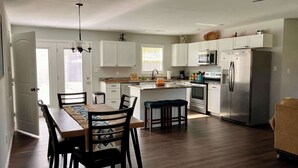 Une cuisine moderne avec des meubles blancs, des appareils en acier inoxydable et un coin repas comprenant une table et des chaises en bois.