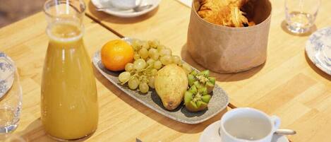Una mesa de desayuno servida con platos, una jarra de jugo, un bol de fruta y una cesta de pasteles.