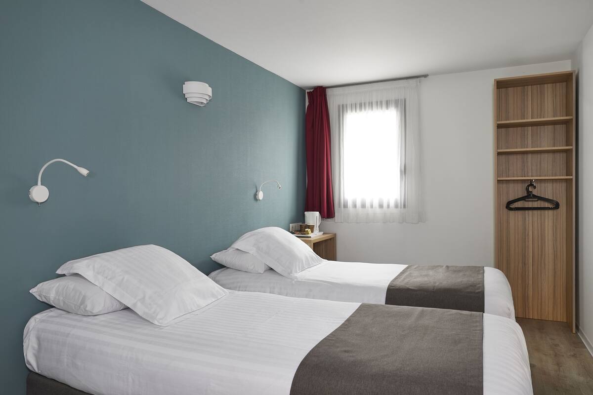 Une chambre d’hôtel avec deux lits, une armoire en bois, une table de chevet et une fenêtre avec des rideaux.