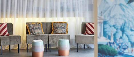 A modern lounge area with a sofa set, patterned cushions, and a mural on the wall.