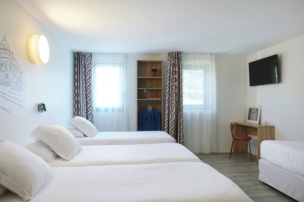 Une chambre d’hôtel avec deux lits, un bureau, une chaise et un téléviseur.
