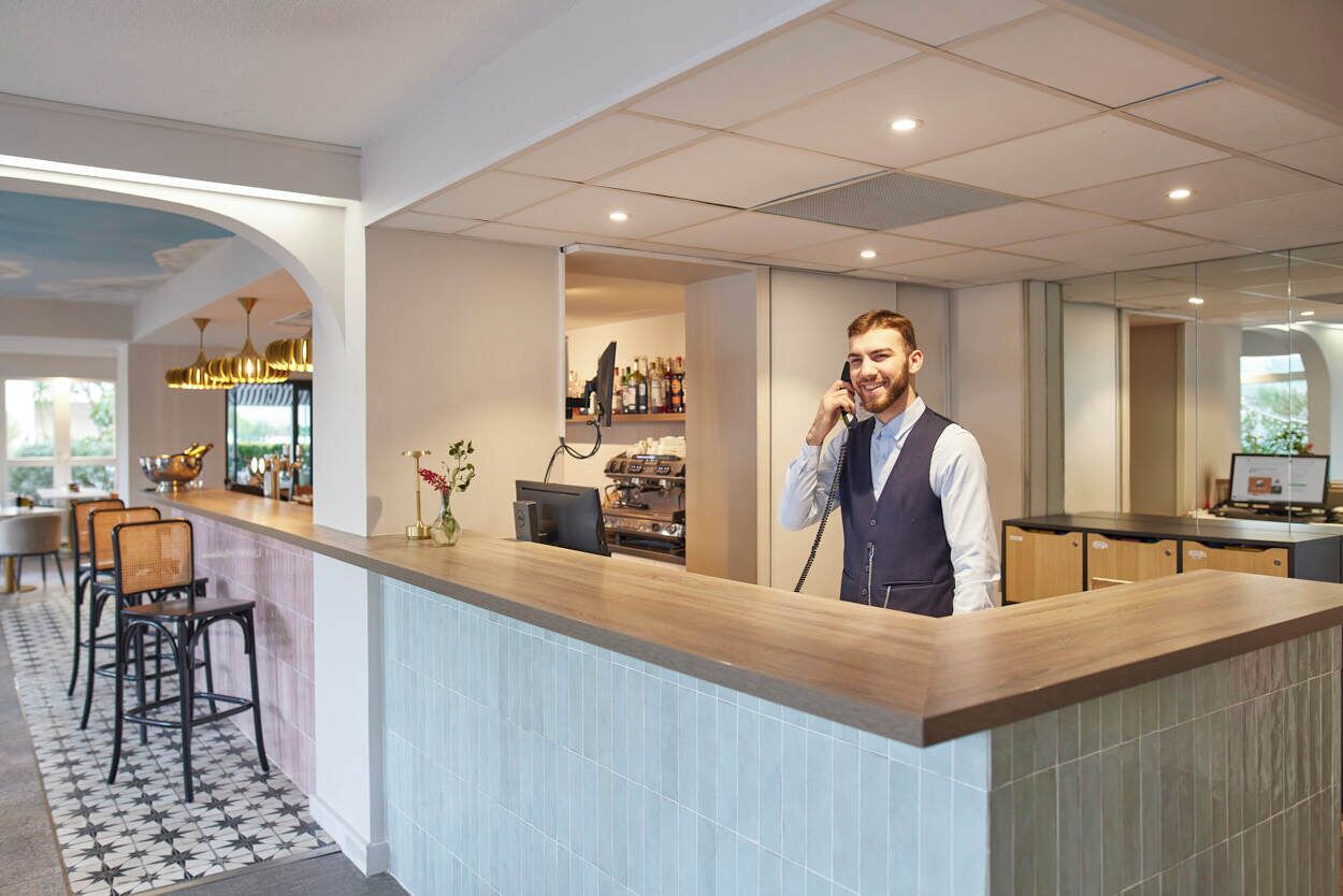 A modern hotel lobby with a reception desk, bar area, and seating.