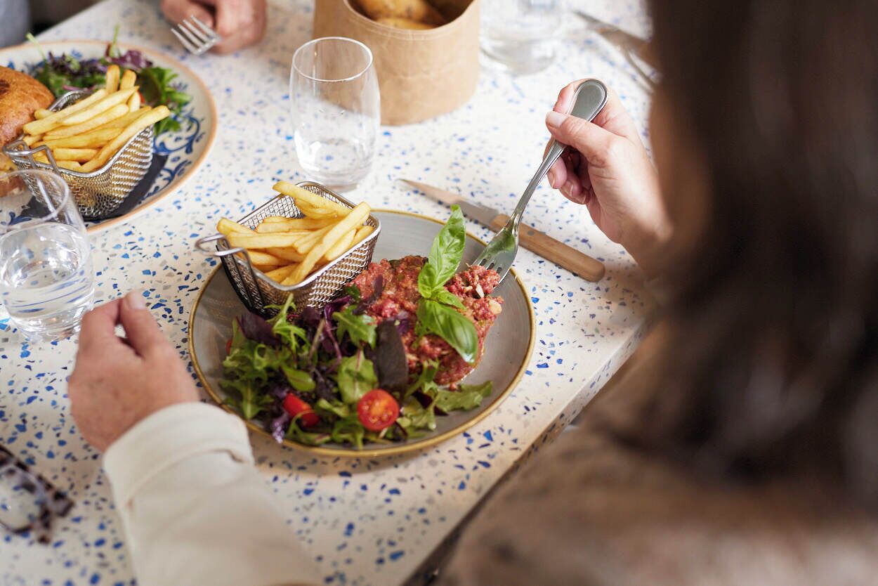 Una mesa de comedor con un plato de comida, una cesta de papas fritas y un vaso de agua.