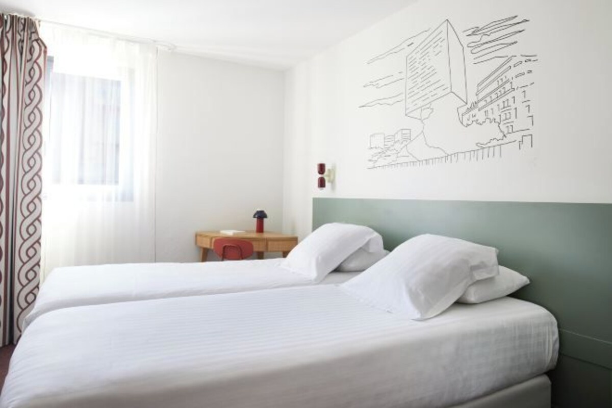 A hotel room with two beds, a desk, and a wall with a cityscape drawing.