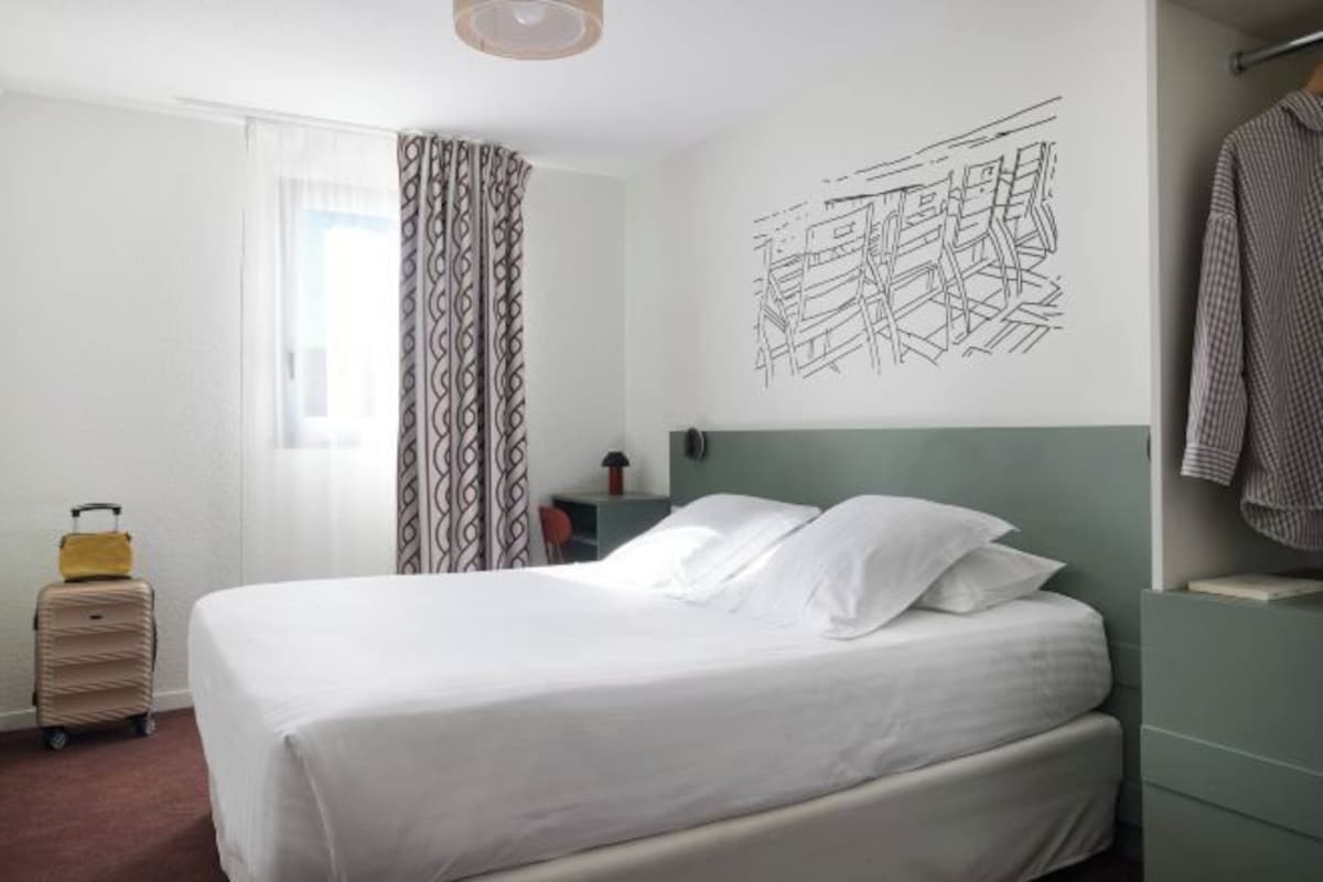 A hotel room with a bed, a suitcase, a window with curtains, and a wall with a geometric design.
