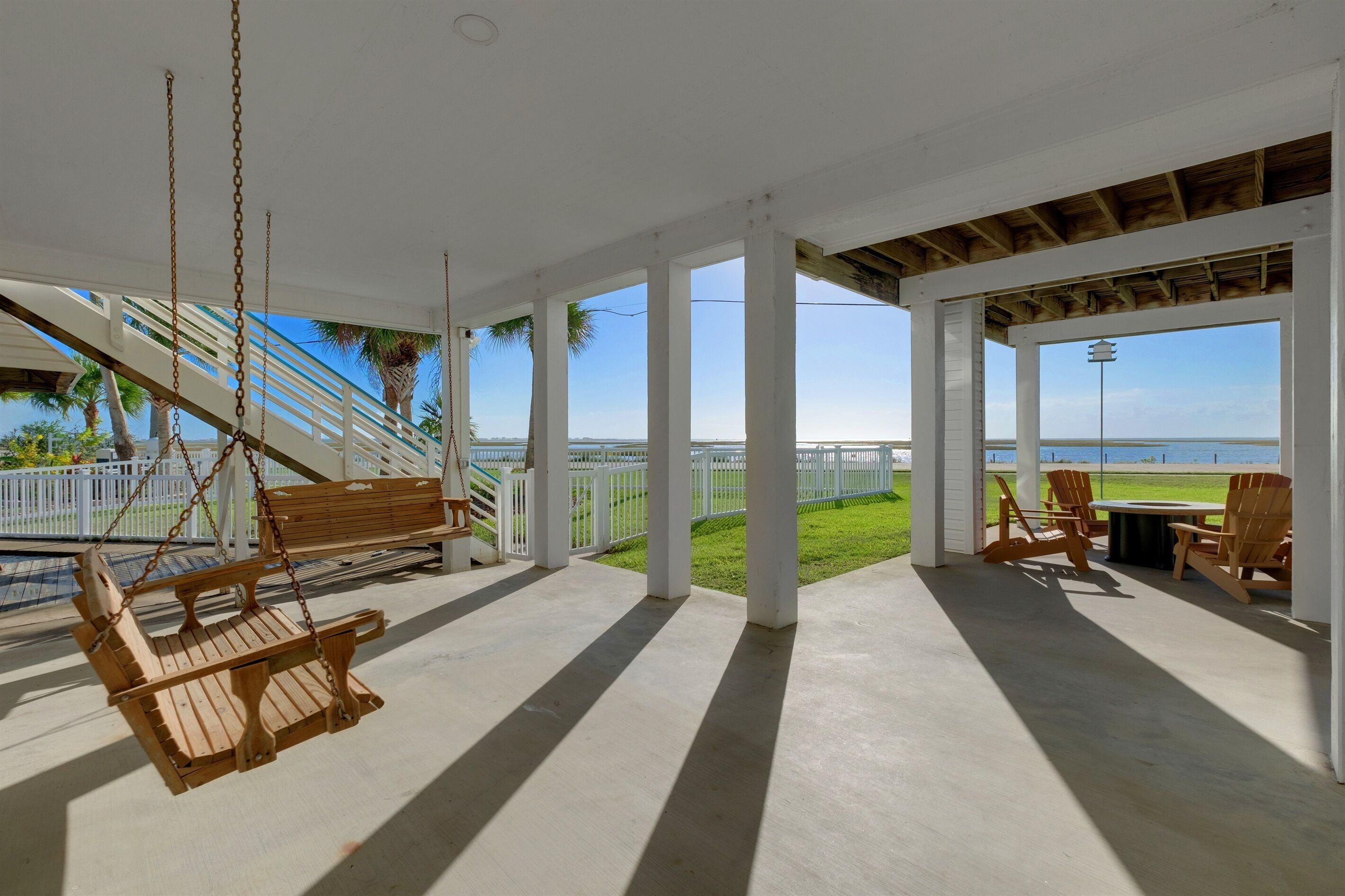 A covered outdoor area with a swing, chairs, and a view of the ocean.