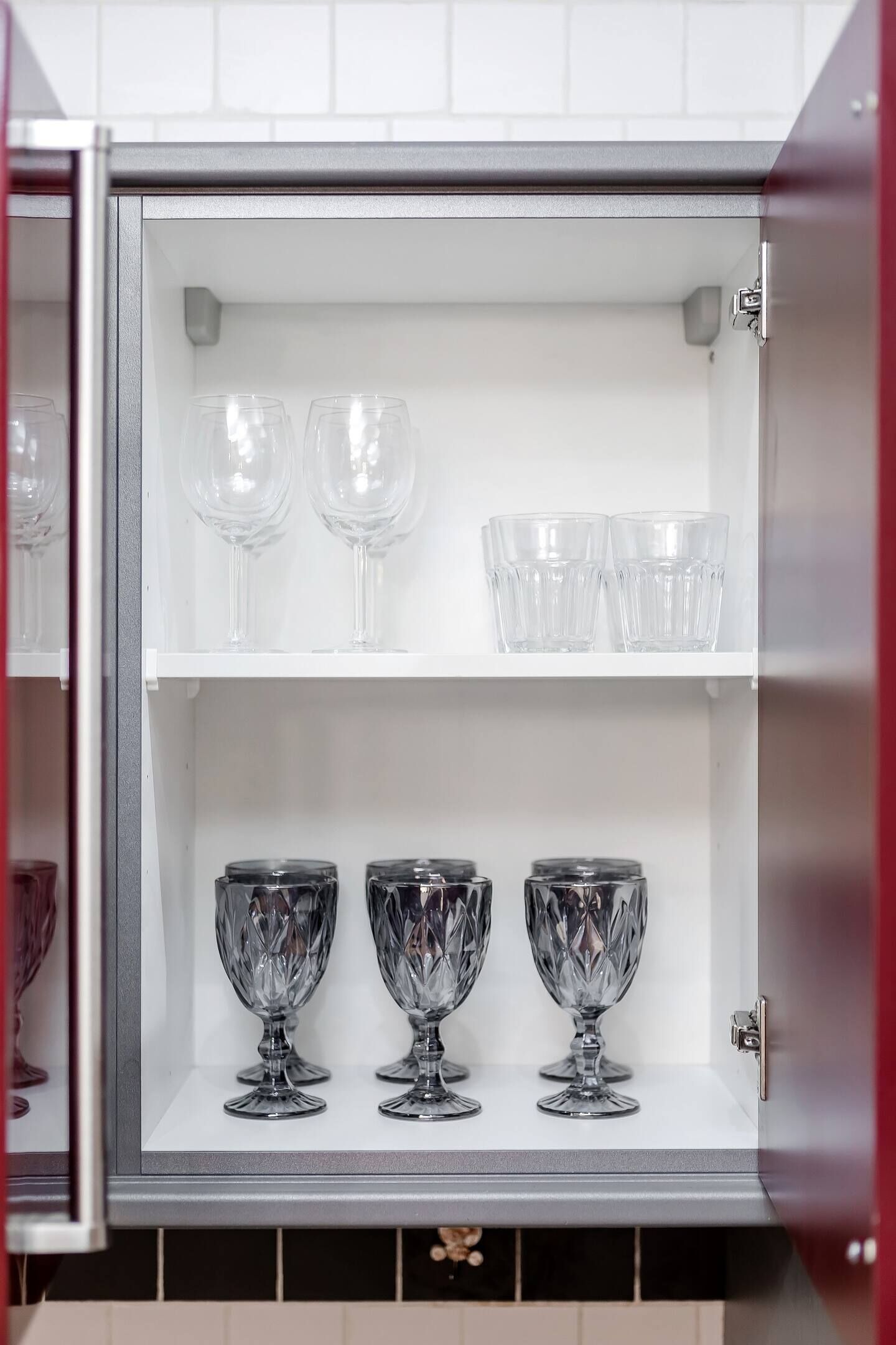 A kitchen cabinet with two shelves, one holding clear wine glasses and the other holding crystal goblets.