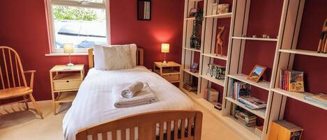 Een slaapkamer met een houten bed, een bureau, een stoel, een boekenkast en een raam met uitzicht.