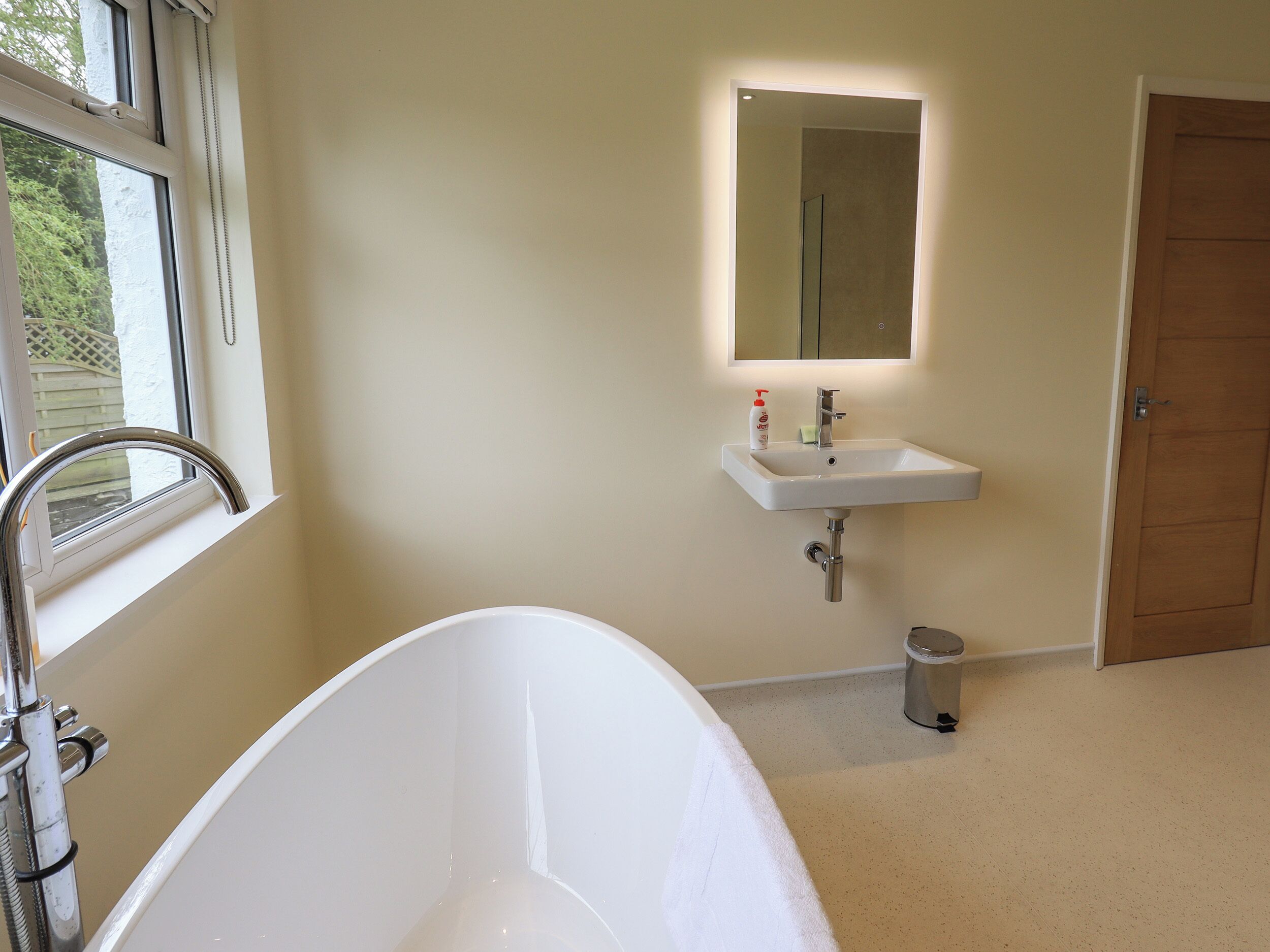 A bathroom with a white bathtub, a sink with a mirror above it, and a door to the right.