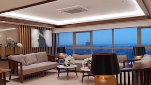 Una sala de estar moderna con un sofá, una mesa de centro y lámparas. Amplias ventanas ofrecen vistas del paisaje urbano.