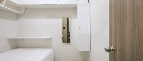 A small, compact room with a bed, a wooden door, and white cabinets.