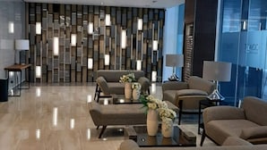 Un vestíbulo moderno con piso pulido, una zona de estar con sofás y una mesa de centro, y una pared decorativa con paneles verticales.