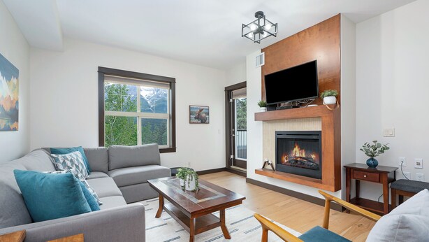 A modern living room with a sectional sofa, a wooden coffee table, and a fireplace. - Heavenly Mountain Condo - Outdoor Hot Tubs & Steam Room (Canmore)