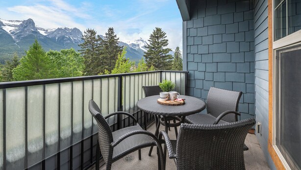 Een balkon met rieten stoelen en een tafel, met uitzicht op een bergachtig landschap.