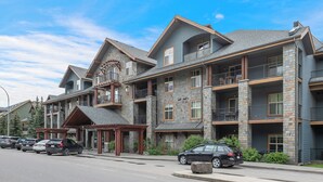 A multi-story hotel with stone facade, balconies, and a covered entrance. - Heavenly Mountain Condo - Outdoor Hot Tubs & Steam Room (Canmore)