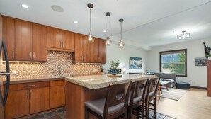 A modern kitchen with wooden cabinets, a large island with bar stools, and pendant lighting. - Heavenly Mountain Condo - Outdoor Hot Tubs & Steam Room (Canmore)