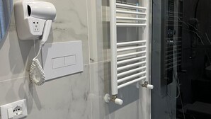 Un baño con lavamanos blanco, espejo, secador de pelo y cabina de ducha de vidrio.