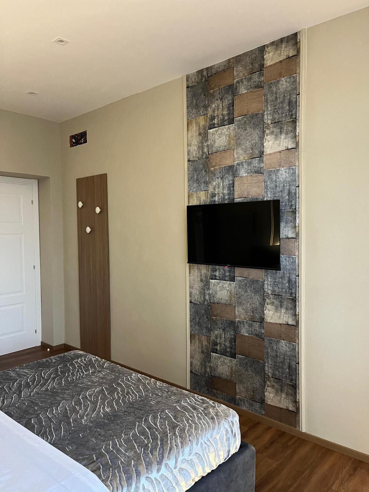 Une chambre à coucher comprenant un lit, une armoire, un téléviseur fixé au mur (qui a une texture particulière) et une porte.