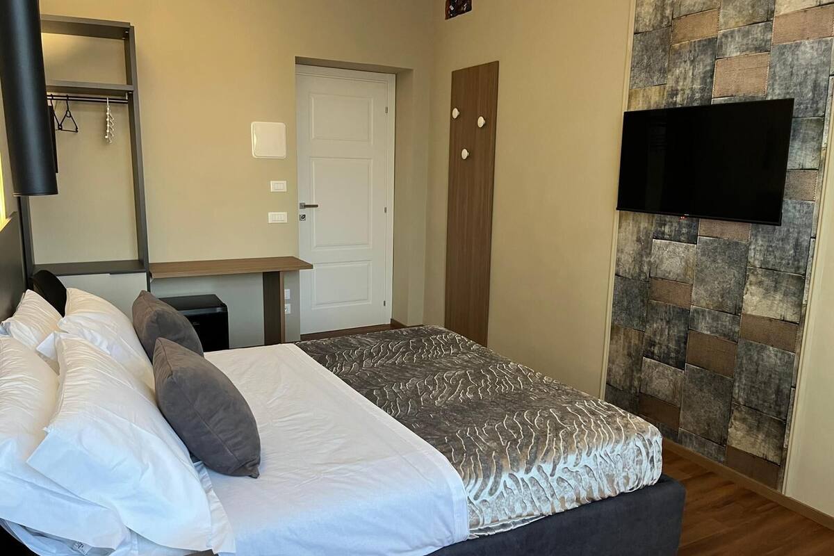 A bedroom with a bed, a flat-screen TV mounted on the wall, a wardrobe, and a door.