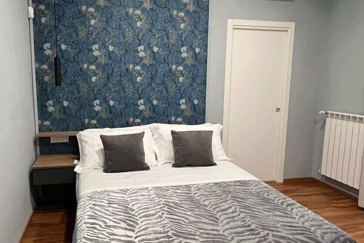 A bedroom with a bed, two pillows, a nightstand, a wooden headboard, a radiator, and a door.