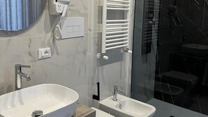 Un baño moderno con un lavamanos ovalado grande, dos bidés, una ducha con mampara de vidrio y un perchero para toallas.