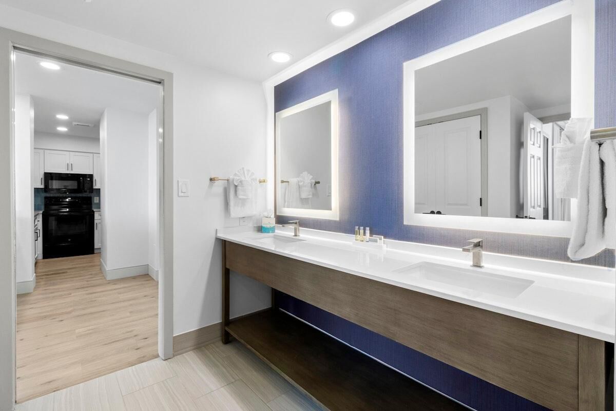 Un baño moderno con un espejo grande, encimera blanca y mueble de tocador de madera.