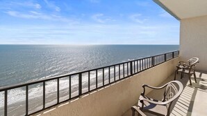 A balcony with a metal railing overlooking a beach. There are two wicker chairs and a small table. - Newly Renovated Coastal Living on the 17th Floor (Myrtle Beach)