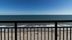 Une vue sur la plage depuis un balcon doté d’une balustrade, avec une plage de sable et l’océan en toile de fond.