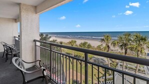 Ein Balkon mit Blick auf den Strand, ein Stuhl und ein Tisch.