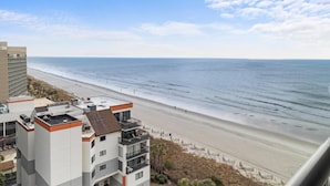 A beachfront hotel with multiple floors, balconies, and a view of the ocean.