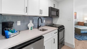 A modern kitchen with white cabinets, a black microwave, and a stainless steel dishwasher.