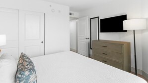 A bedroom with a bed, a dresser, a television mounted on the wall, and a door leading to another room.