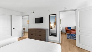 A hotel room with a bed, a dresser, a TV, a mirror, and a seating area with a chair and a table.