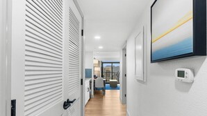 A hallway with white walls, a wooden floor, and a view to a dining area with a table and chairs.