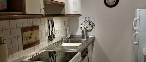 A kitchen with a stove, sink, and white cabinets. There is a clock on the wall and a sign with a cow image.