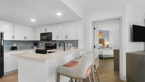 Une cuisine moderne avec des meubles blancs, un îlot central doté de tabourets, un four à micro-ondes et un évier.