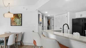 A modern kitchen with white cabinets, a black refrigerator, and a dining area with a wooden table and chairs. - 7th Floor Beachfront Getaway in Two Bedroom Bliss (Myrtle Beach)