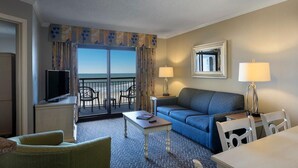 Ein Hotelzimmer mit Balkon, einer Couch, einem Fernseher, einem Tisch und einer Lampe.