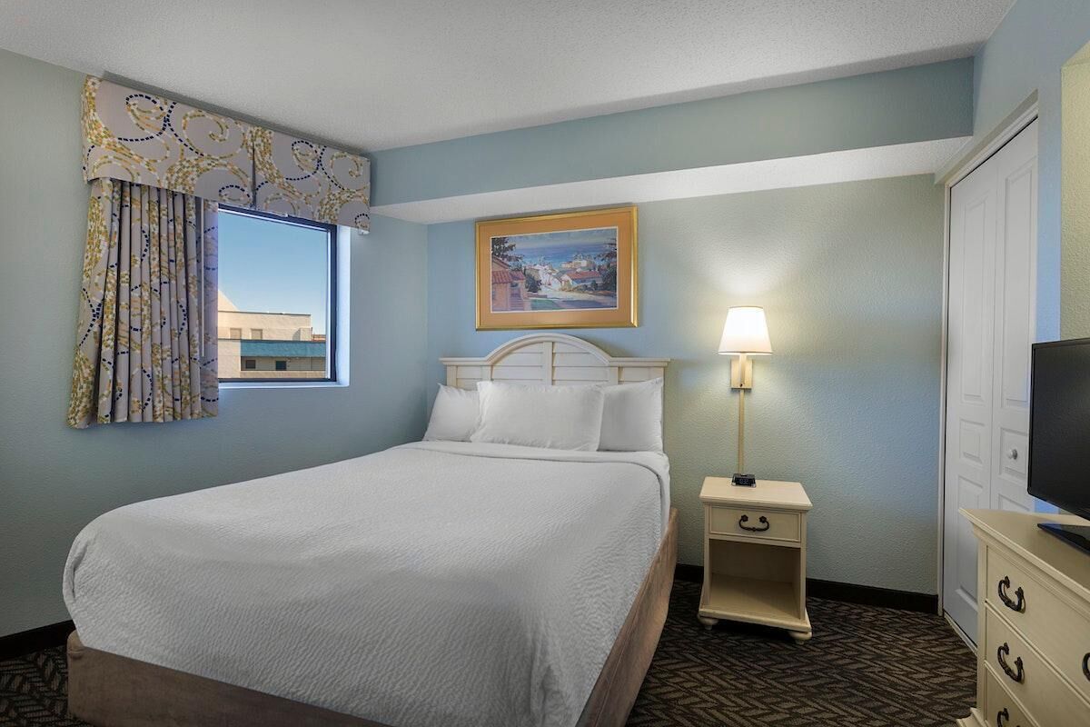 Une chambre d’hôtel avec un lit, une table de chevet avec une lampe, une commode, un téléviseur et un tableau au mur.