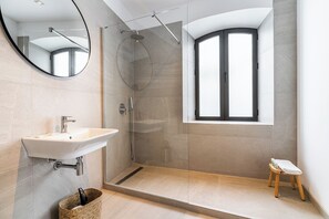 A modern bathroom with a glass-enclosed shower, a sink with a mirror, and a small stool. - Arena House Conil (Conil de la Frontera)