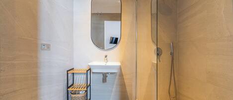 A modern bathroom with a glass shower enclosure, a white sink, and a small wooden shelf with baskets.